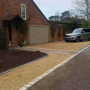 A gravel driveway with a parked car in front, surrounded by greenery.